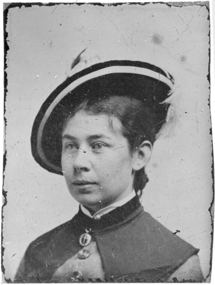 A close black-and-white portrait of a young woman in a feathered hat, scratched and specked across the surface