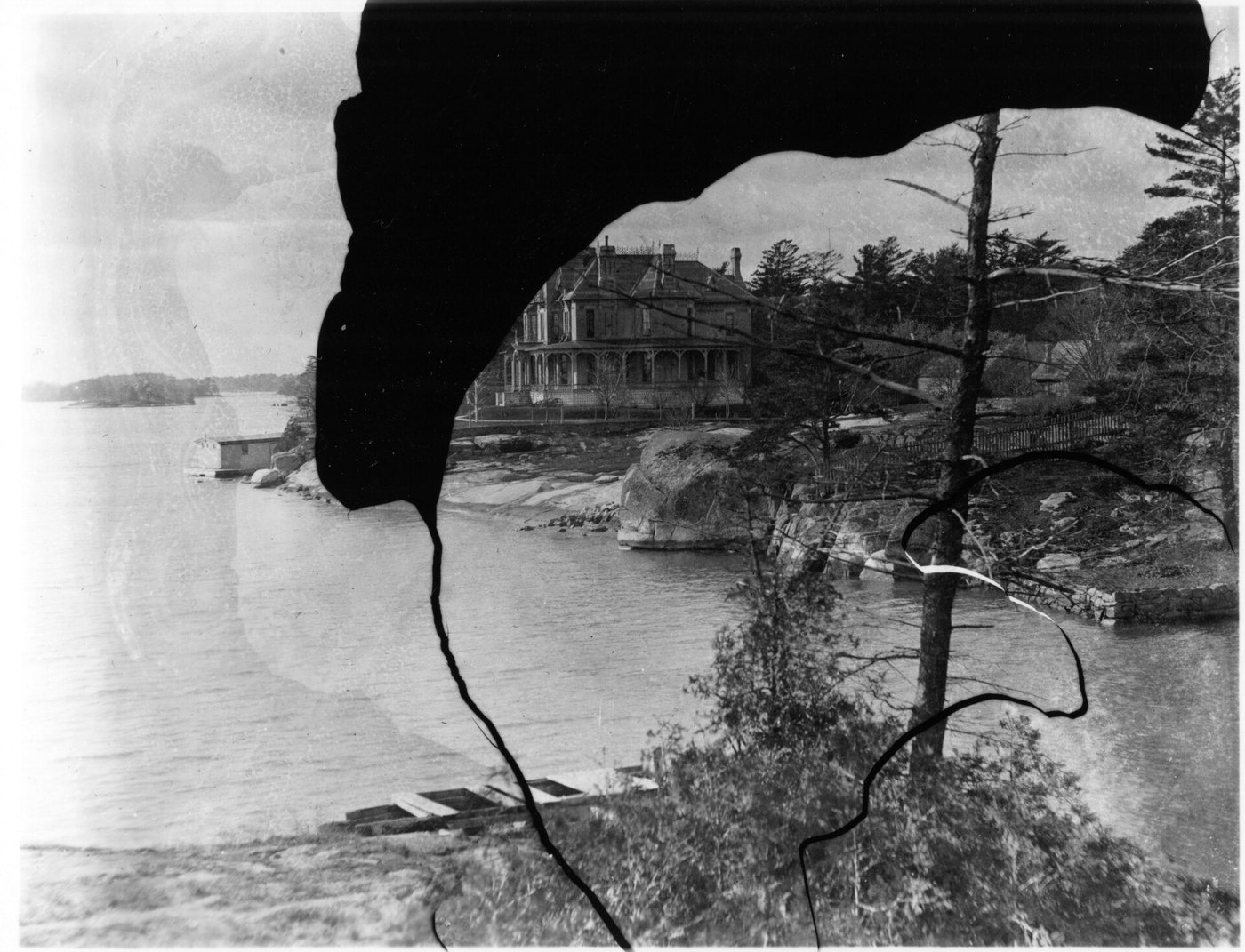 A black-and-white view of a house above a lake, with a large irregular area of the picture lost to black