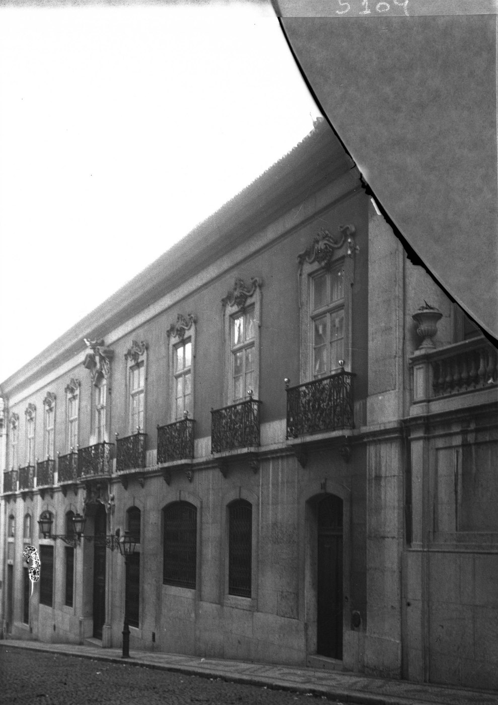 A glass plate photograph of a building front, with a curved area missing from the upper right