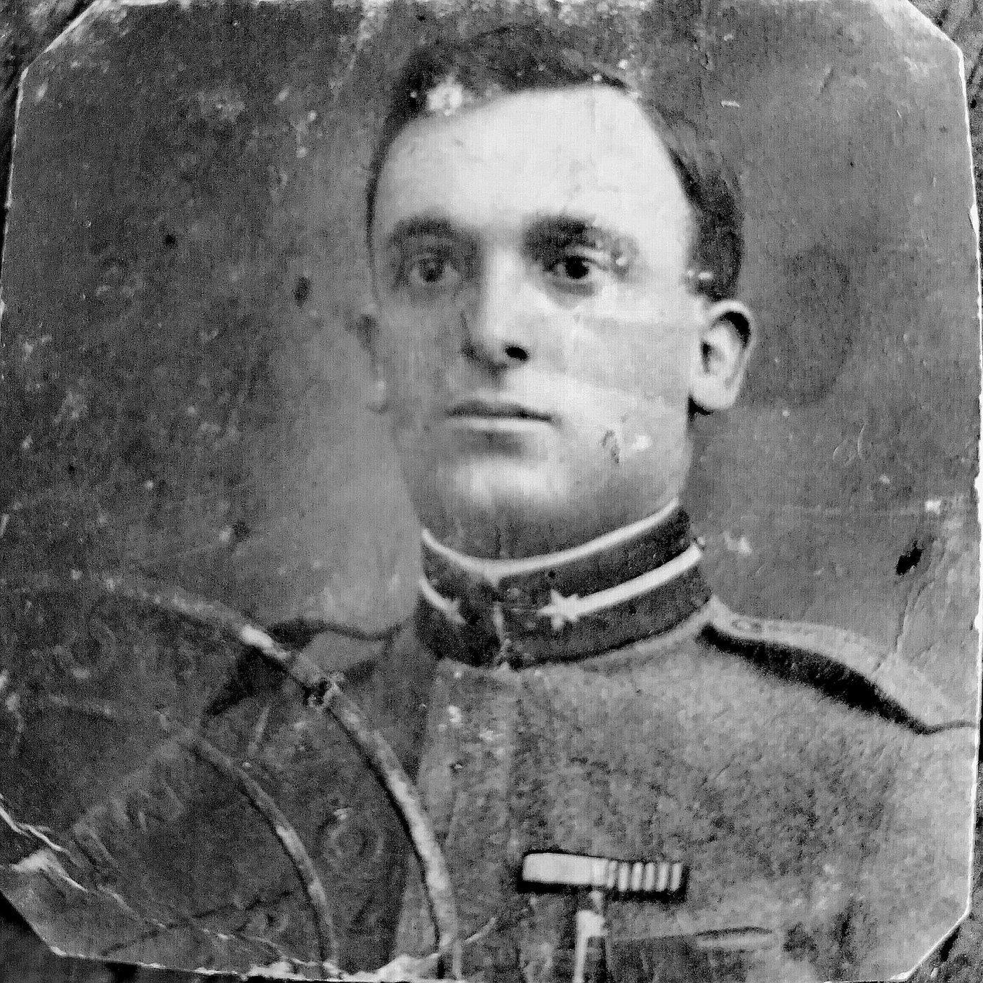 A black-and-white portrait of a young soldier, the surface abraded and cracked across the whole print
