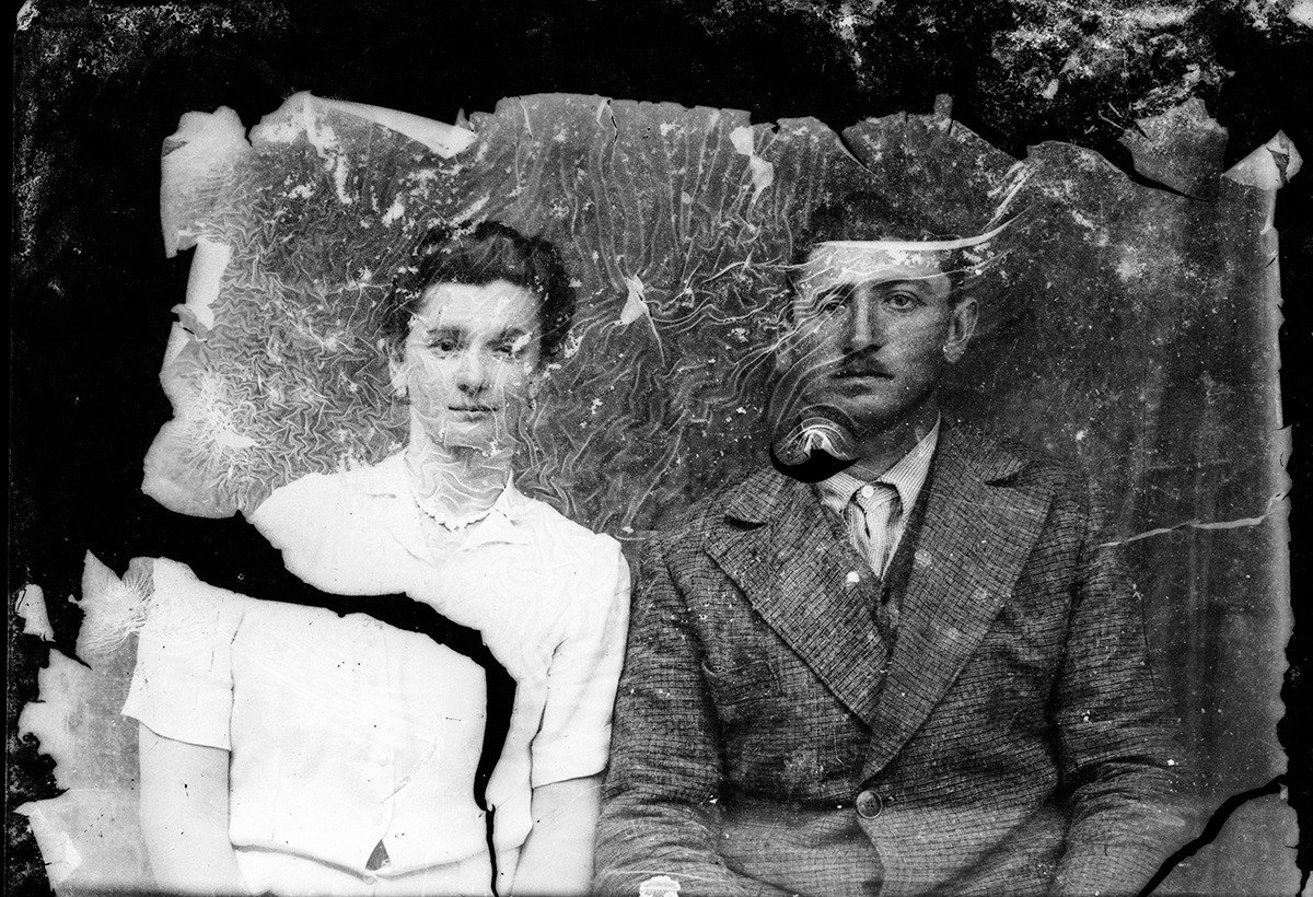 A black-and-white portrait of a seated couple, the emulsion crazed and flaking over most of the print