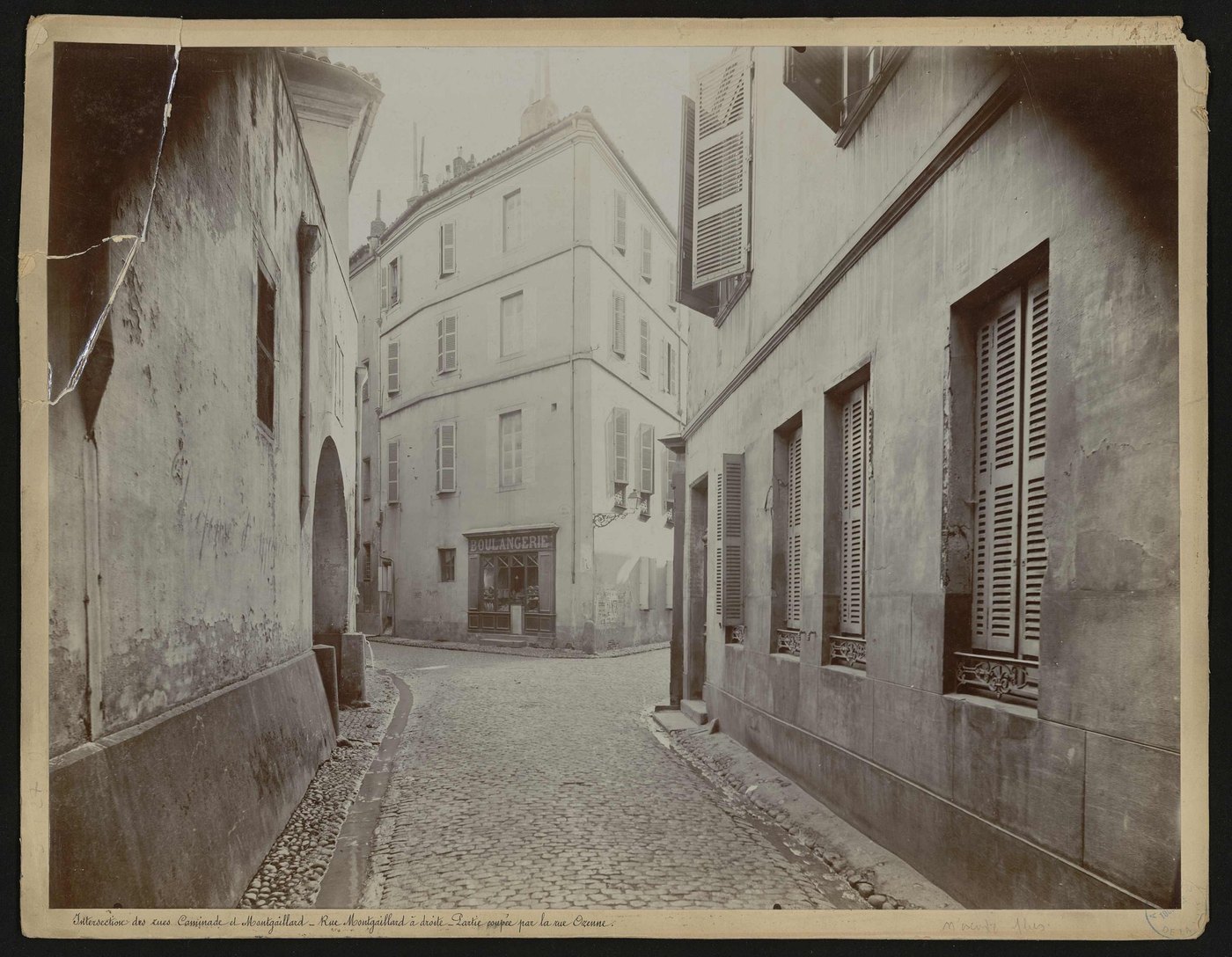 A photograph of a narrow street corner with a bakery, a long split running through the upper left